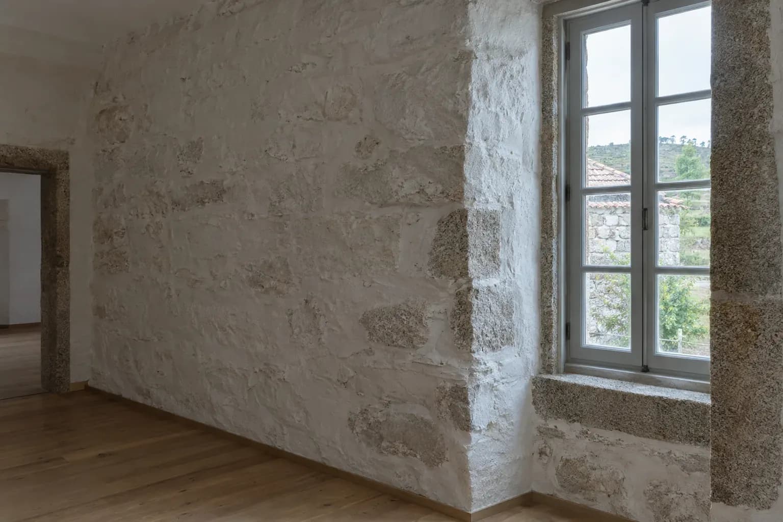 Parede de pedra caiada numa casa antiga, com uma janela e um pavimento de madeira