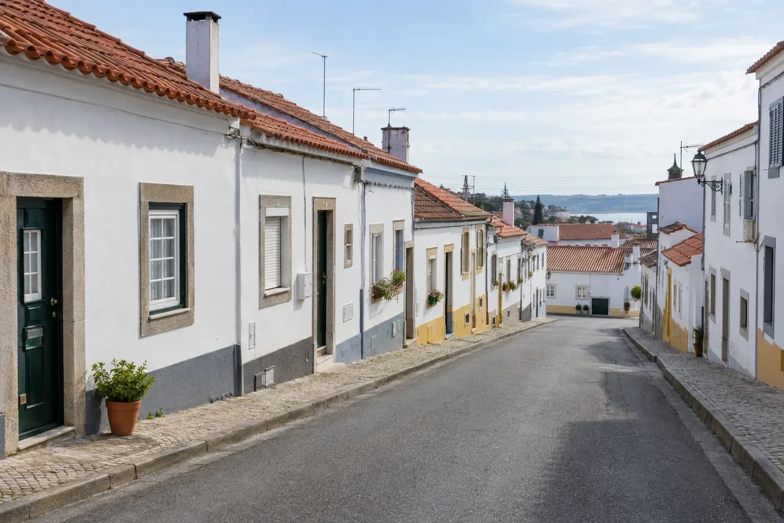 Rua residencial com casas brancas e telhados de telha, numa vila portuguesa.