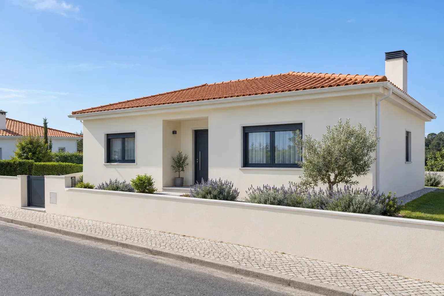 Moradia de um piso com fachada de reboco claro e muro baixo, numa rua residencial.