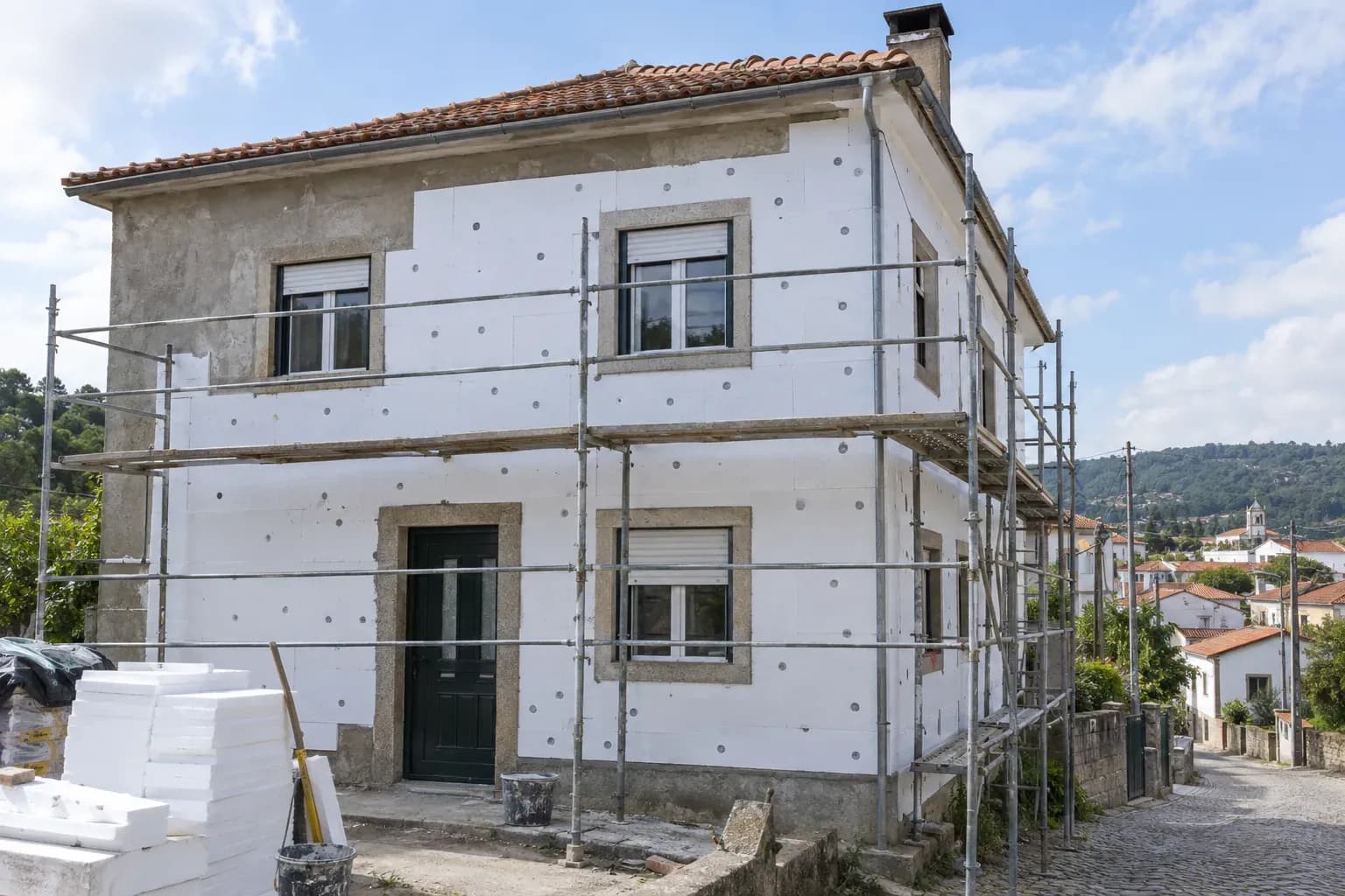 Fachada de uma moradia de dois pisos em obra de capoto, com placas brancas de isolamento e andaime.